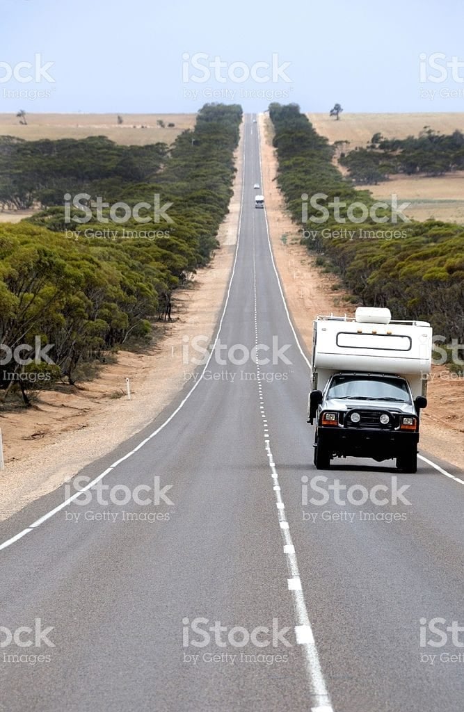 A slide-on camper travelling a long straight highway through open scrub