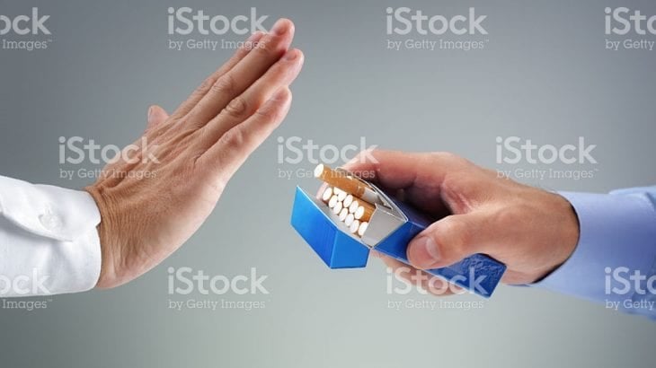 A raised hand refusing a cigarette offered from an open pack