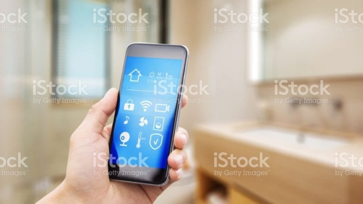 A hand holding a smartphone showing a home-control app