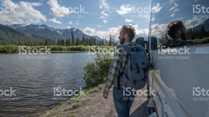 A traveller with a backpack standing beside a campervan at a mountain lake