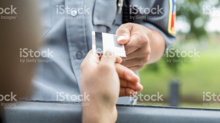 A driver handing a licence card to an official through a car window