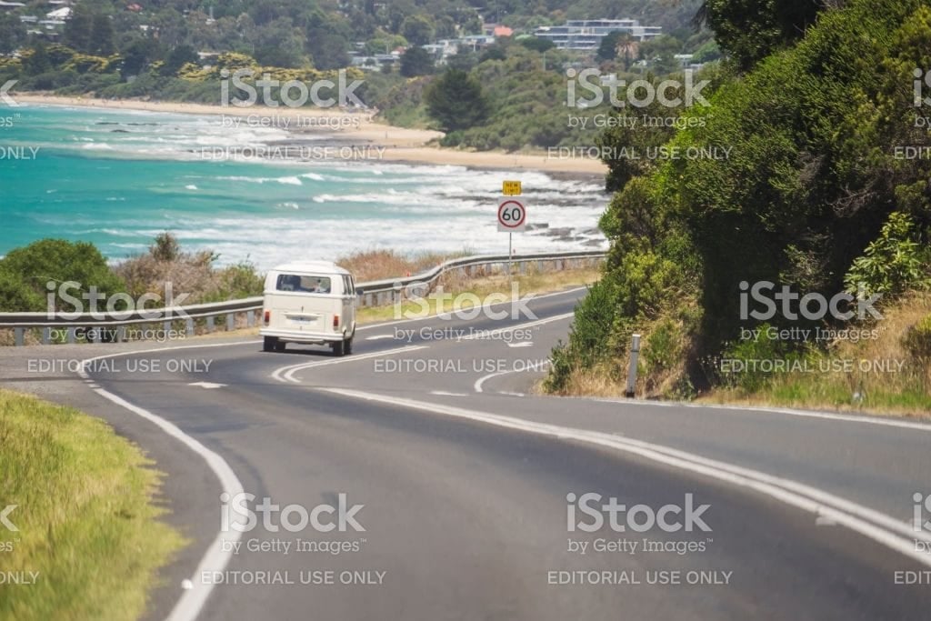 A classic campervan on a winding coastal road above a beach